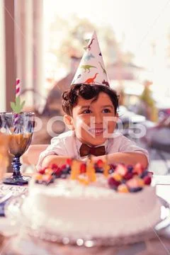 Cute birthday boy wearing party hat and sitting with cake Stock Photos