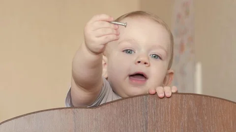 Cute blond babe shows playing in a baby crib with a bolt. He smiles and twists Video stock 75054334