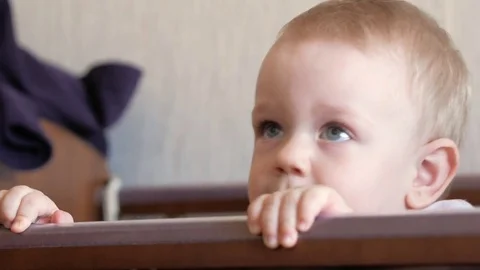 Cute blond babe shows playing in a baby crib with a bolt. He smiles and twists Stock Footage 75054441