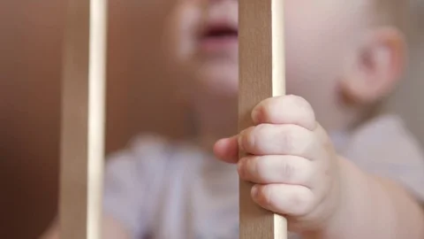 Cute blond babe shows playing in a baby crib. In focus, the hand holds on to Stock Footage 75054582