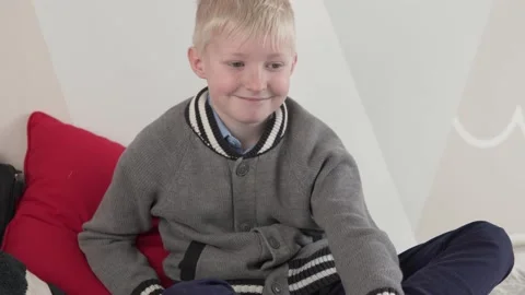 A cute blond boy of 10 years sits on the sofa and smiles Stock Footage 151886086