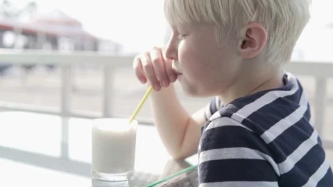 Cute blond boy drinks a milkshake in a cafe on a hot summer day Stock Footage 119212689