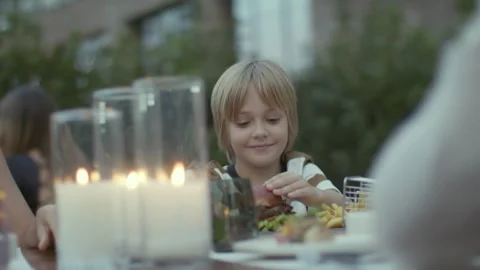 Cute Blond Boy Eating Burger at Family Candlelit Dinner Table 4K 動画素材 344057063
