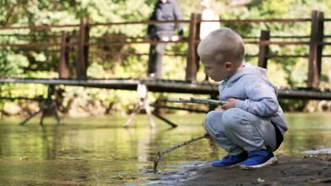 Cute blond boy playing on the river bank during a family vacation. Stock Footage 250455712