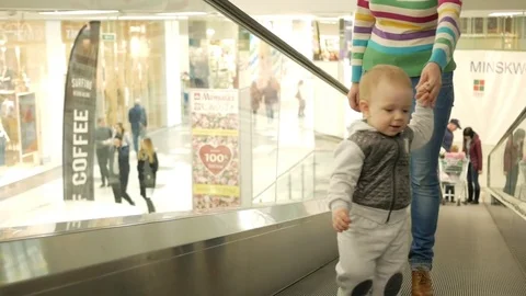 A cute blond boy of two years with his mother climbs the escalator in a large Video stock 75052390