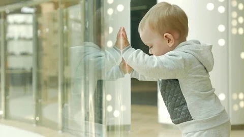 A cute blond boy of two years is considering a store through the glass. The kid Video stock 75053050