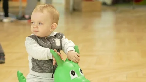 Cute blond boy two years old jumping on an inflatable horse in the mall Stock Footage 75053510