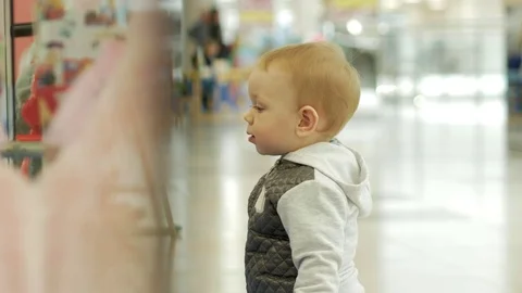A cute blond boy of two years is considering a store through the glass. The kid Video stock 75053973