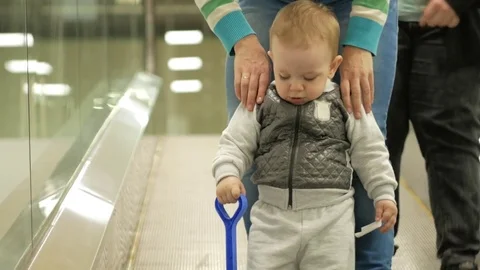 A cute blond boy of two years with his mother climbs the escalator in a large Stock Footage 75054173