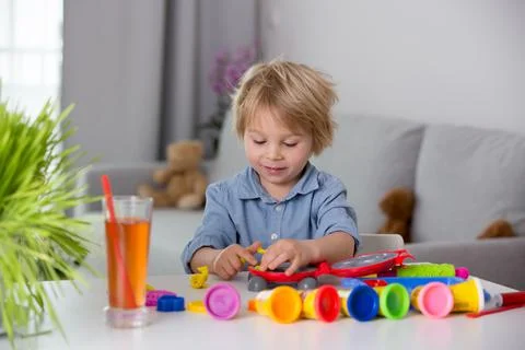 Cute blond child, boy, playing with play doh modeline at home, making differe Stock Photos