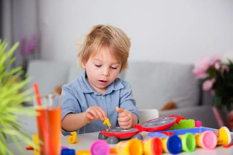 Cute blond child, boy, playing with play doh modeline at home, making differe Stock Photos