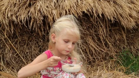 Cute blond girl eats corn flakes with milk from a glass jar. Video stock 76739893