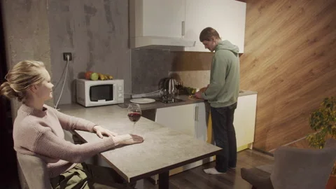 Cute blonde came to visit her friend, the guy makes a salad, she drinks wine in Stock Footage 145085520