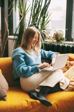 Cute blonde sitting on the couch and working at the computer. The girl checks Foto stock