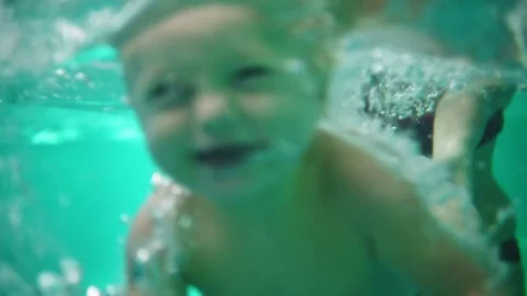 Cute blonde toddler is diving under the water while his mother is holding him Stock Footage 81539802