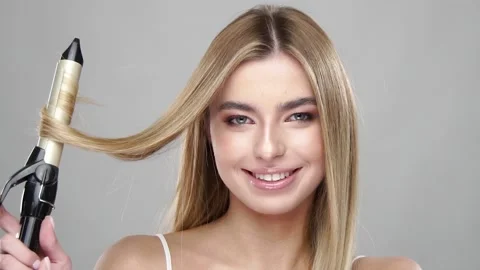 Cute blonde using curling iron and smiling Stock Footage 146598420