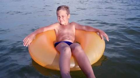 A cute boy 6-7 years old swinging on the sea waves on an inflatable ring Video stock 159469644