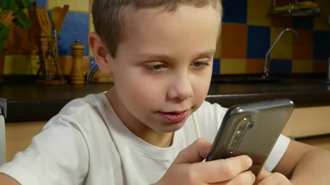 Cute boy 6-7 years old smiling and talking while looking at the smartphone Stock Footage 168557865