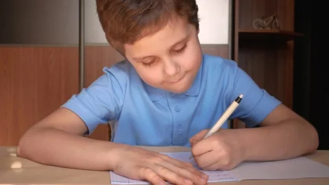 A cute boy of 6-7 years old writes with a pen in a notebook. distance schooling Stock Footage 170592166