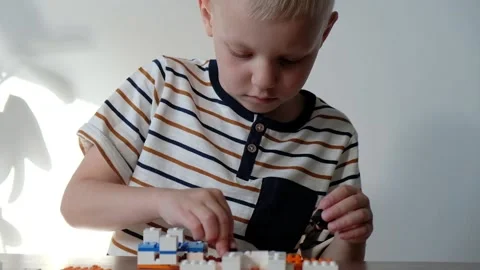 Cute boy 6 years old playing with colorful plastic toy bricks at the table at Vídeo Stock 108653413