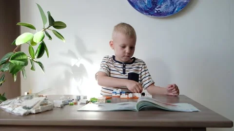 Cute boy 6 years old playing with colorful plastic toy bricks at the table at Stock-Footage 108653470