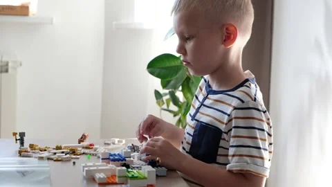 Cute boy 6 years old playing with colorful plastic toy bricks at the table at Vidéo 108654000