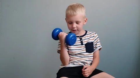 Cute boy 6 years old doing exercises with dumbbell on gray background Stock Footage 111368758