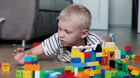 Cute boy 6 years old playing with colorful plastic toy bricks on the floor at Stock Footage 111389400