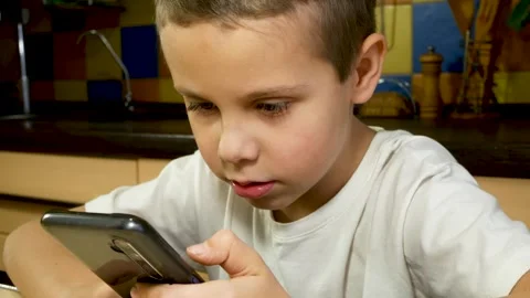 A cute boy of 7-8 years old is sitting with a gadget in his hands, communicating Stock Footage 273938287