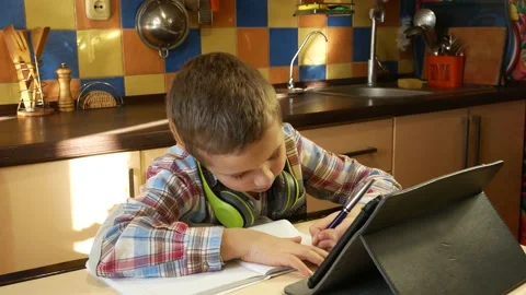 A cute boy of 7 years old sits in the kitchen at the table, looks at the desktop Stock Footage 168607729