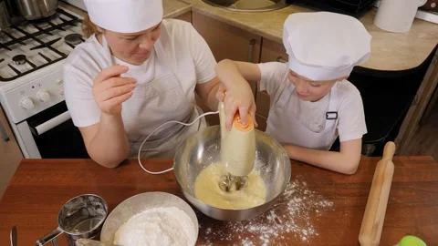 A cute boy in an apron and a cap beats dough for cookies on his own with a mixer Stock Footage 279379802