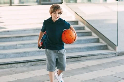 A cute boy with a backpack in one hand and a basketball in the other. The boy Stock Photos