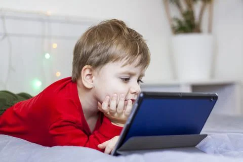 A cute boy is on the bed looking at a tablet. Online training, communication  Stock Photos