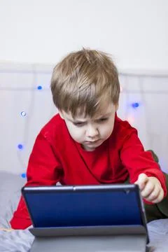 A cute boy is on the bed looking at a tablet. Online training, communication  Stock Photos