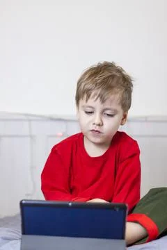 A cute boy is on the bed looking at a tablet. Online training, communication  Stock Photos