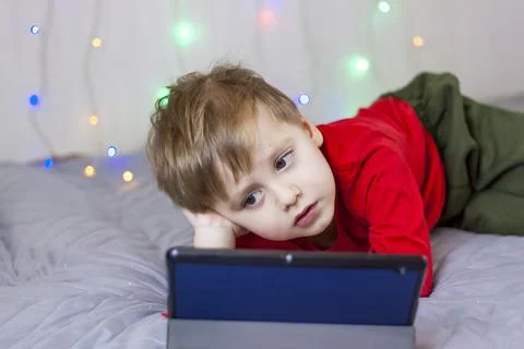 A cute boy is on the bed looking at a tablet. Online training, communication  Stock Photos