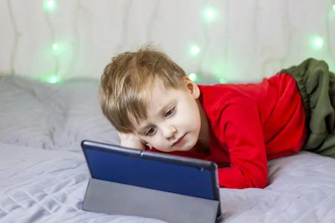 A cute boy is on the bed looking at a tablet. Online training, communication  Stock Photos