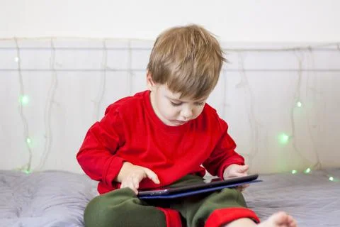 A cute boy is on the bed looking at a tablet. Online training, communication  Stock Photos