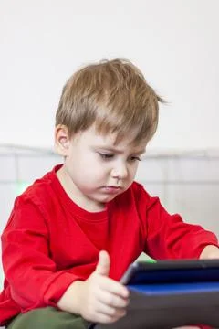 A cute boy is on the bed looking at a tablet. Online training, communication  Stock Photos