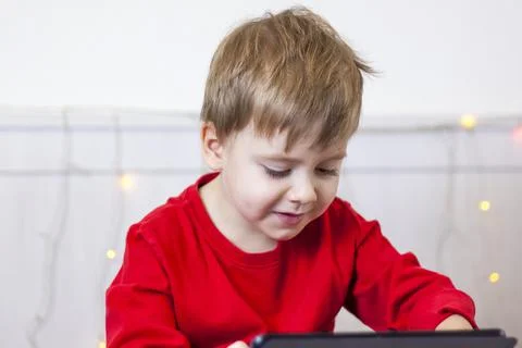 A cute boy is on the bed looking at a tablet. Online training, communication  Stock Photos