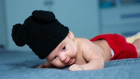 Cute boy in black hat of Mickey Mouse and red pants put on the bed. Stock Footage 169039309