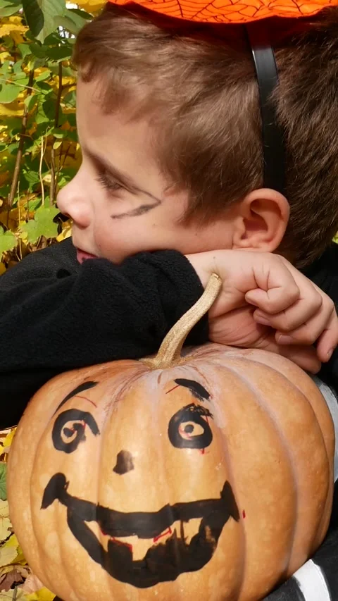 A cute boy in a black suit and with a painted pumpkin in his hands sits Stock Footage 317849385