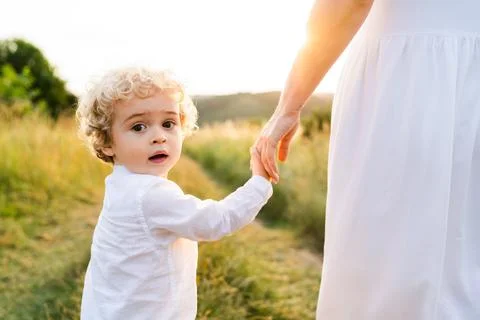 Cute boy with blond curly hair walks with his mother along a picturesque fiel Stock Photos
