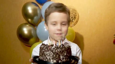 A cute boy blows out the candles on the cake on his birthday. In the background Stock Footage 234552247