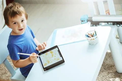 Cute boy in blue tshirt using digital tablet or computer for drawing his picture Stock Photos