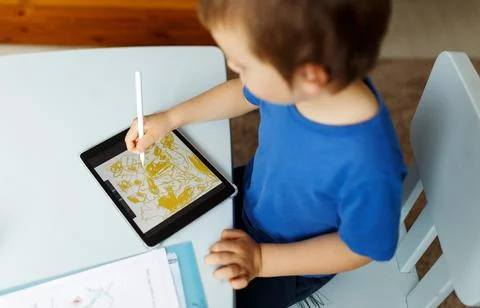 Cute boy in blue tshirt using digital tablet or computer for drawing his picture Stock Photos