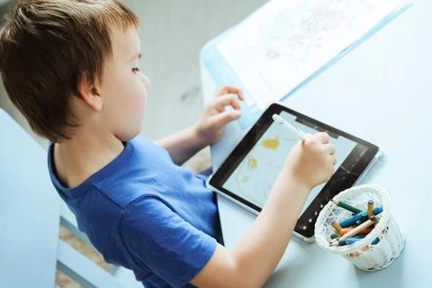 Cute boy in blue tshirt using digital tablet or computer for drawing his picture Stock Photos