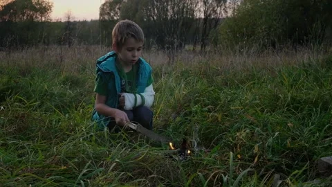 Cute boy with a broken arm lights a fire Stock Footage 153325643