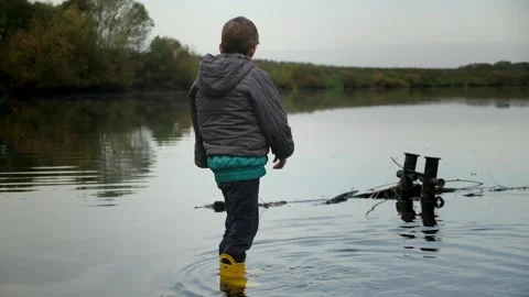 A cute boy with a broken arm stands in the water and looks down Stock Footage 153325233