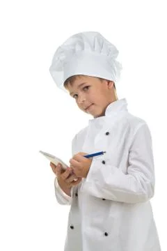 Cute boy chef writes down a recipe into a notebook, on white background. Stock Photos
